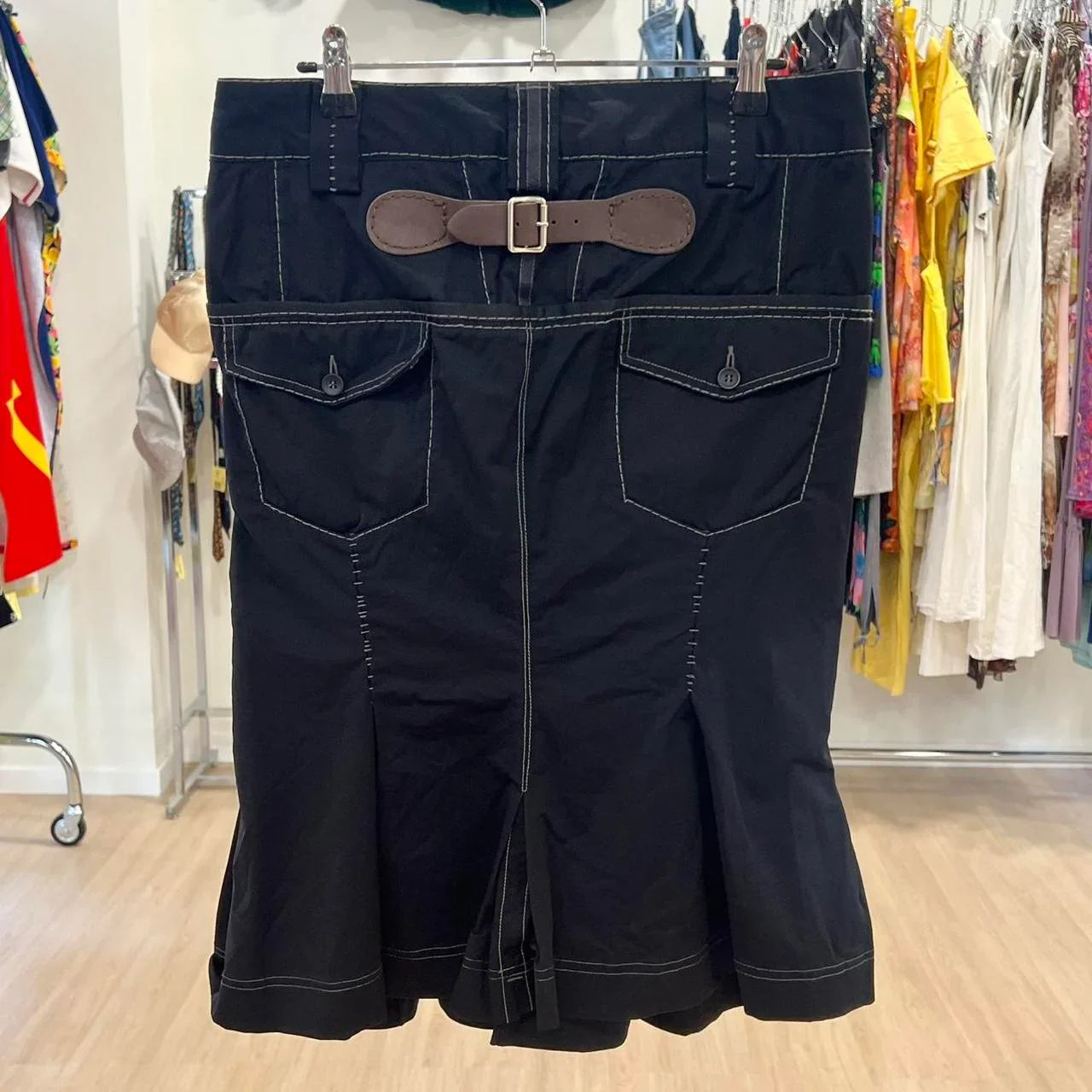 Black skirt with white contrast stitching, front pockets, and brown belt, displayed in store