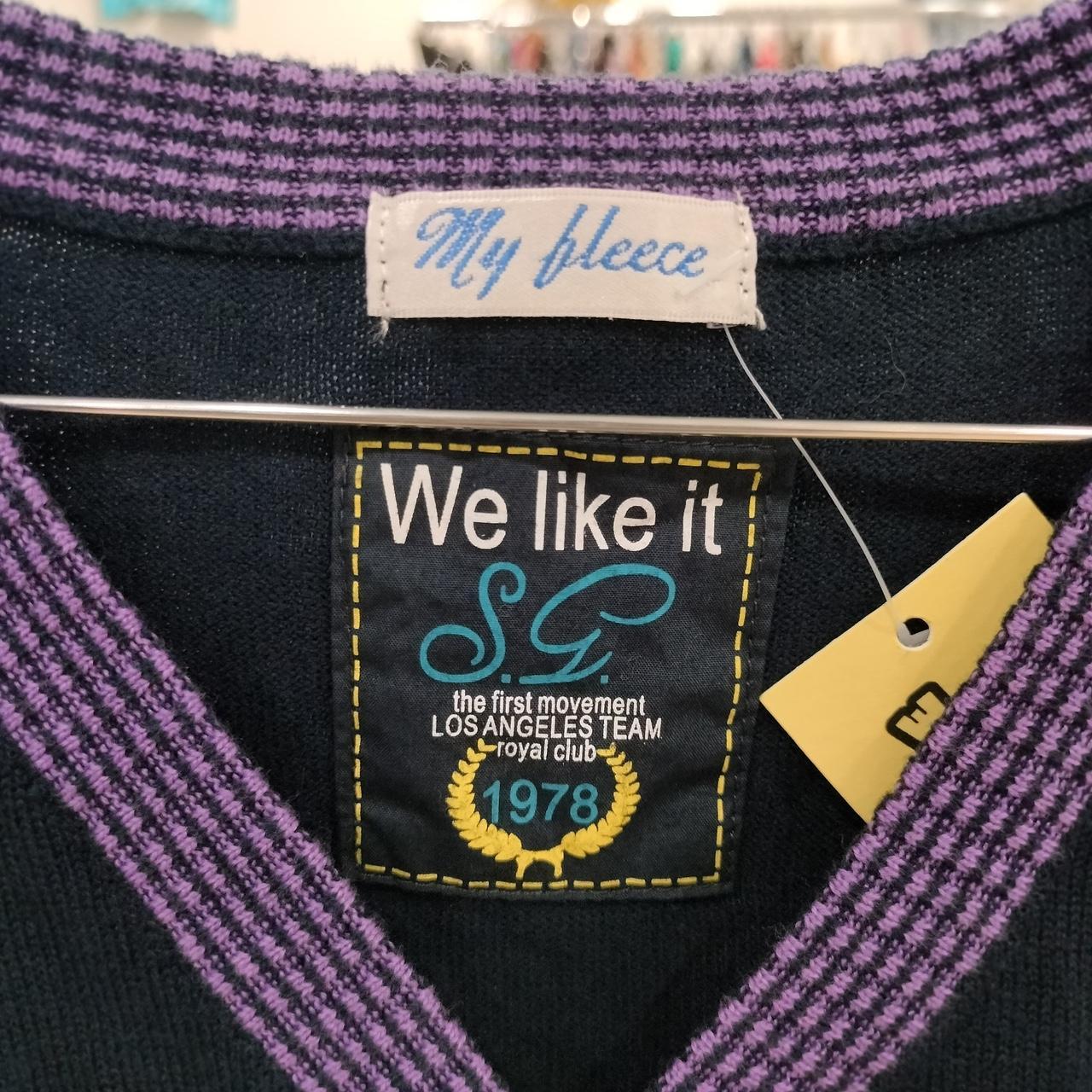 Close-up of a sweater label with purple ribbed collar, text 'My fleece' and 'We like it'.