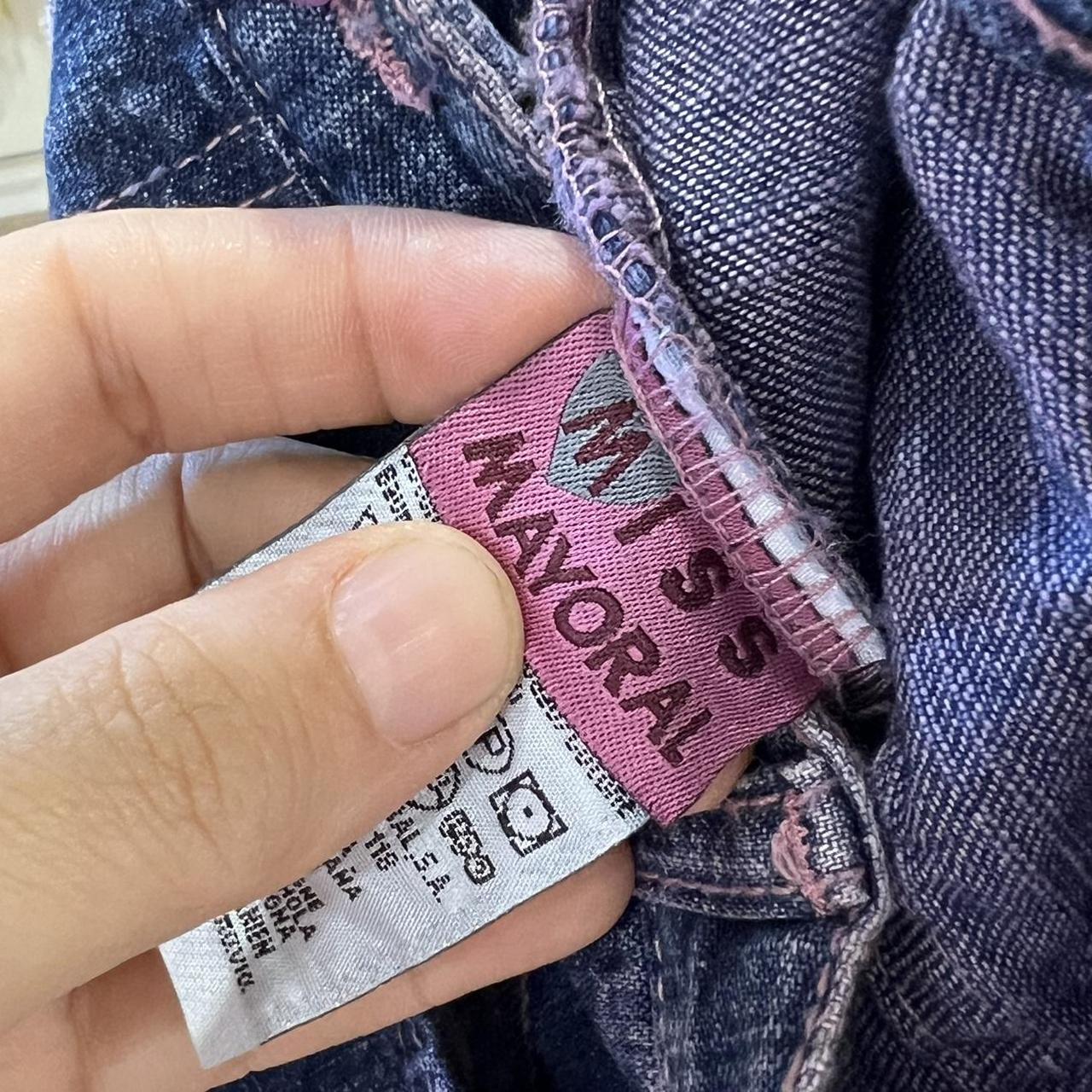 Hand holding a pink label on denim fabric with 'Mayoral' branding