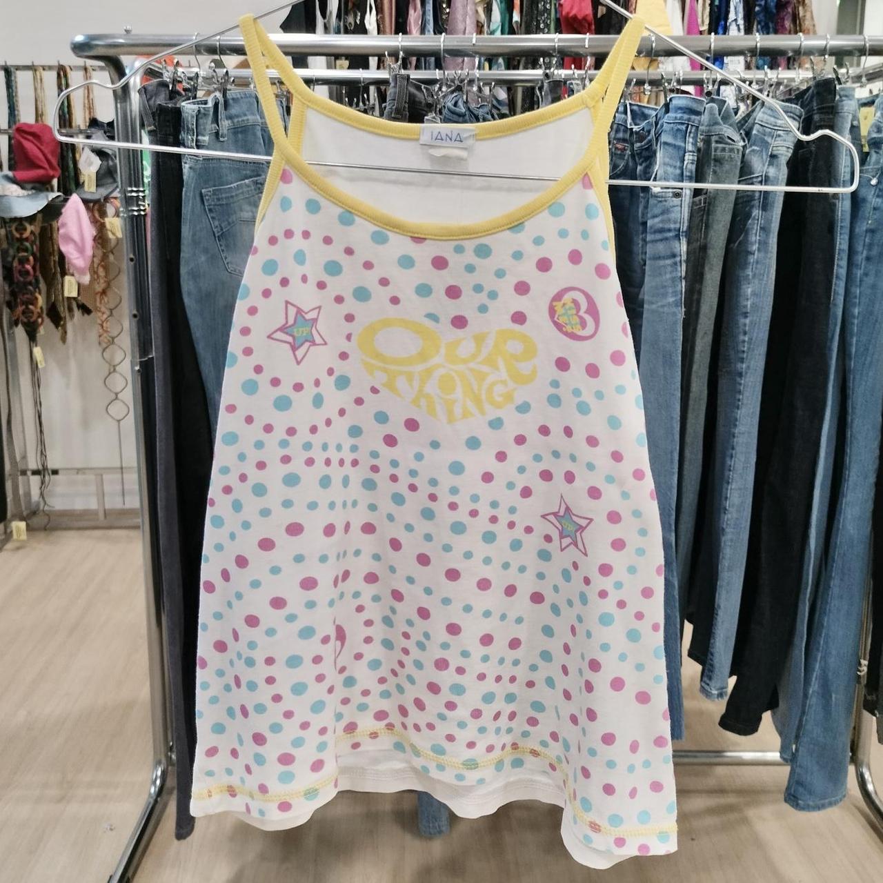 Colorful polka dot tank top with yellow trim and 'Our Thing' text, hanging in a thrift store