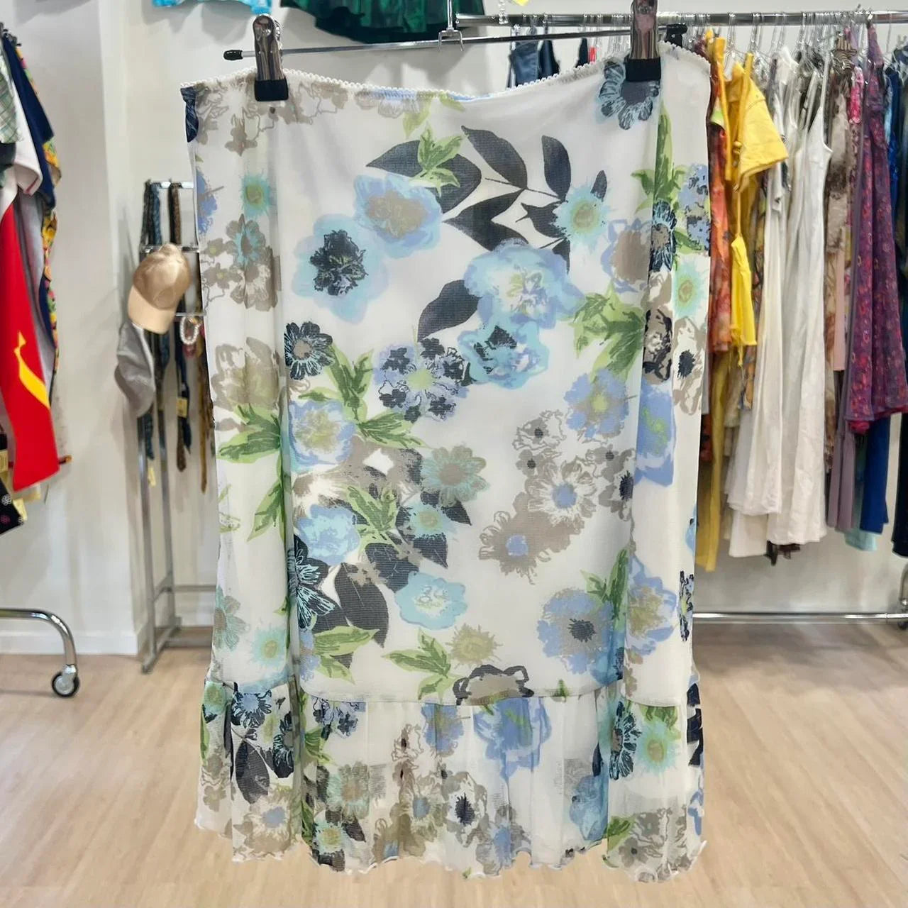 sheer white floral skirt with blue and green flowers hanging in a thrift clothing store