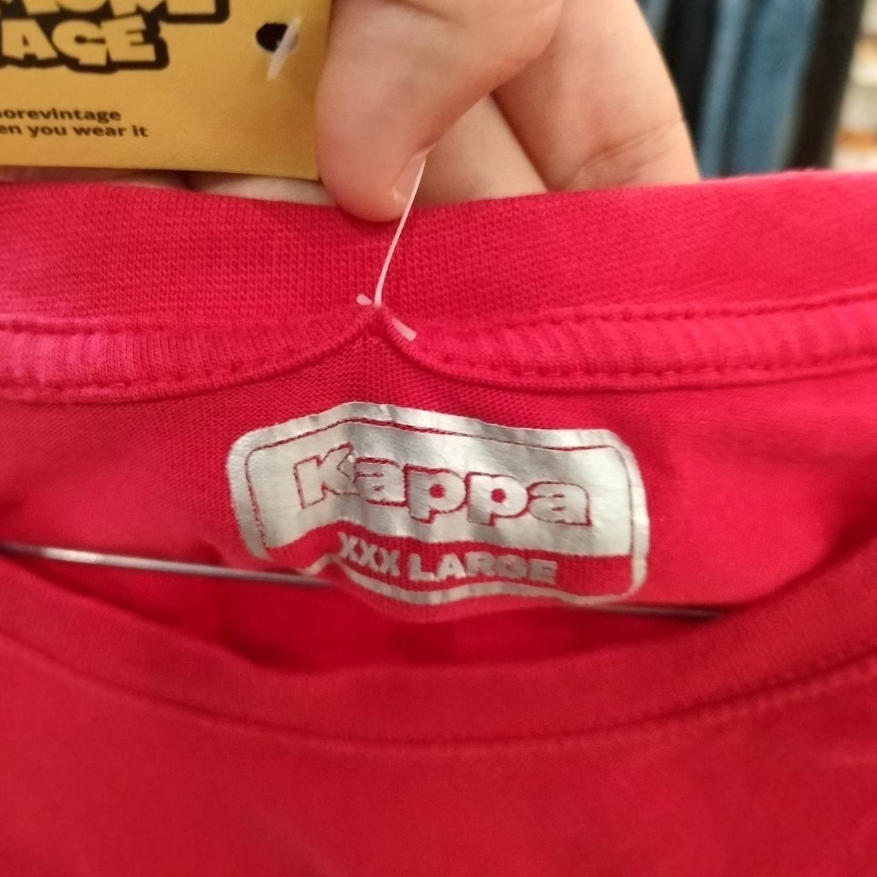 Close-up of a red sleeveless top with a Kappa logo and a hand holding a yellow tag