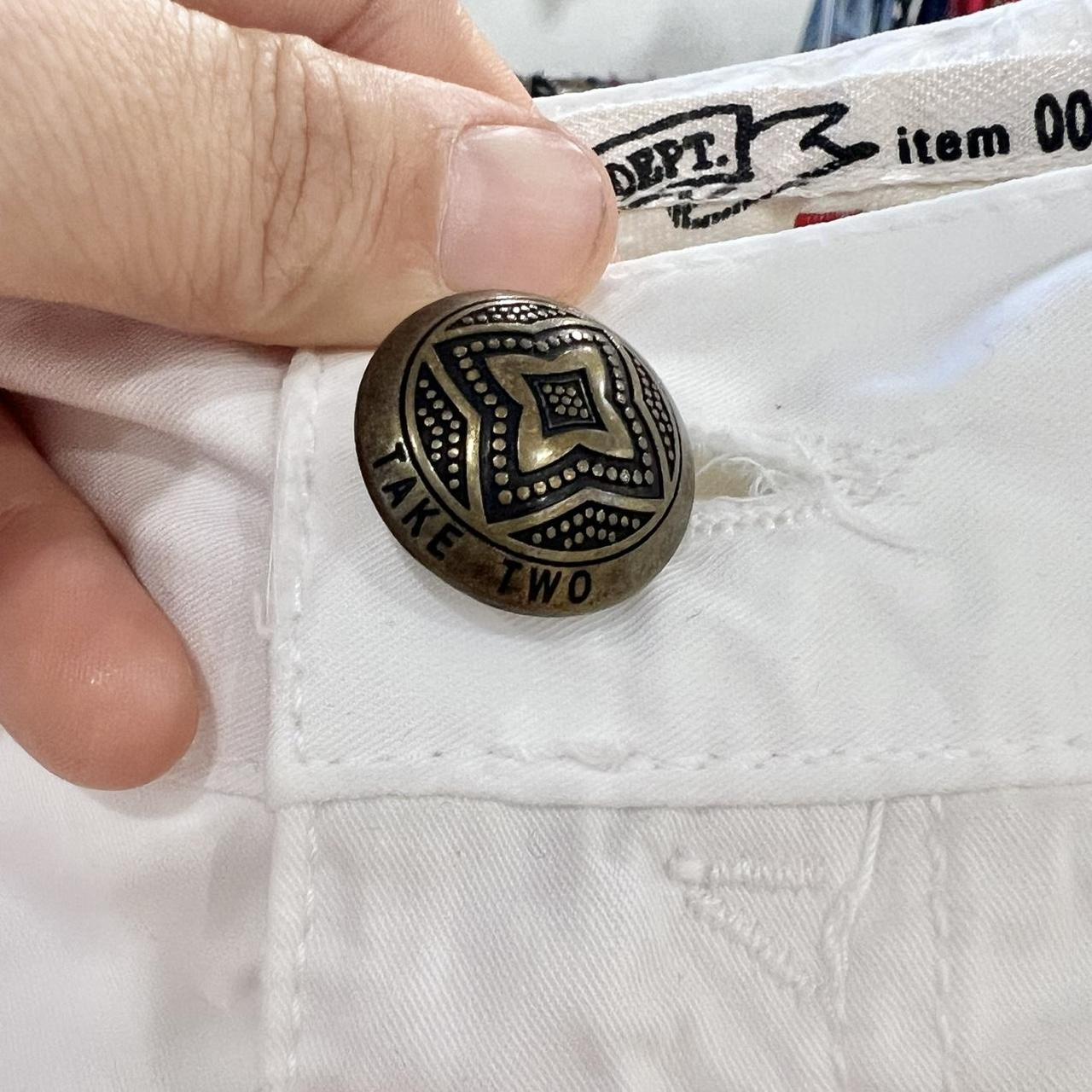 Close-up of vintage brass button on white denim with unique pattern and 'TAKE TWO' embossing.