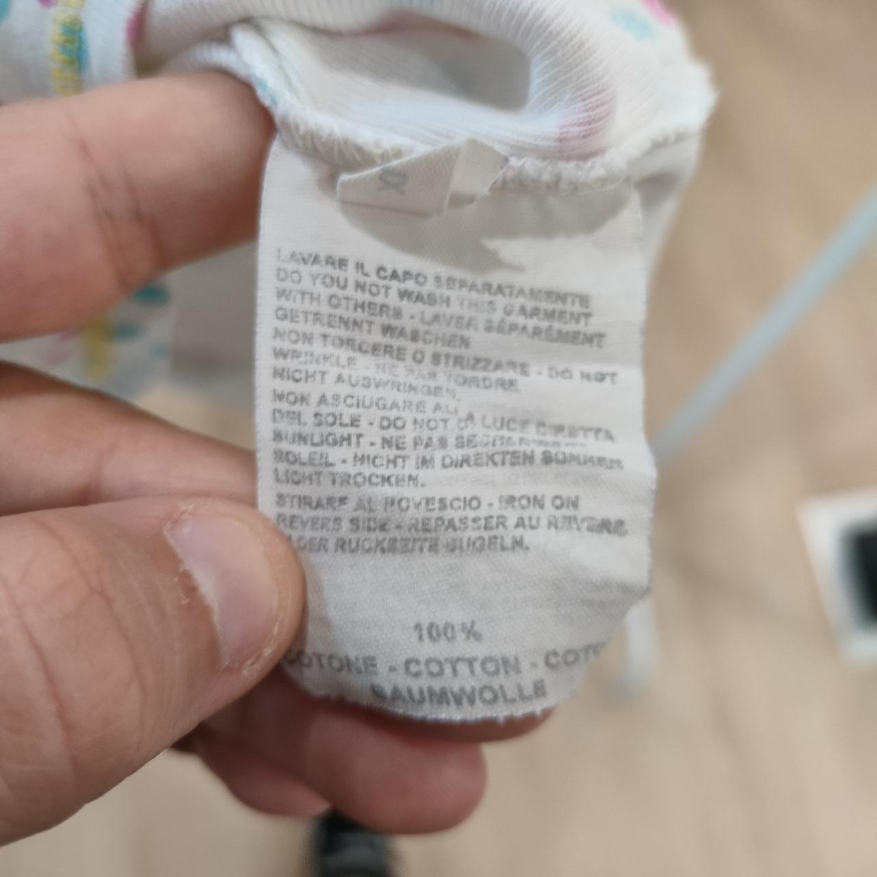 Hand holding a white clothing care label with multi-language washing instructions and 100% cotton text.