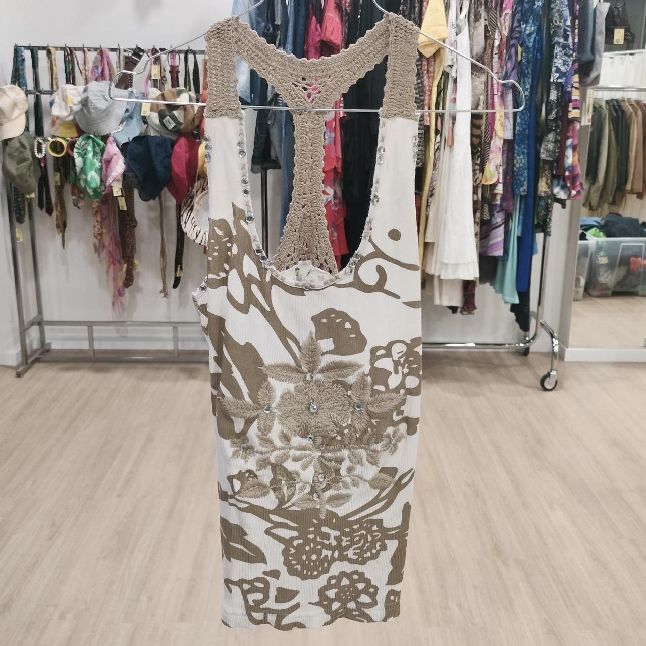 Beige and white crochet racerback tank top with floral embroidery on hanger in thrift shop