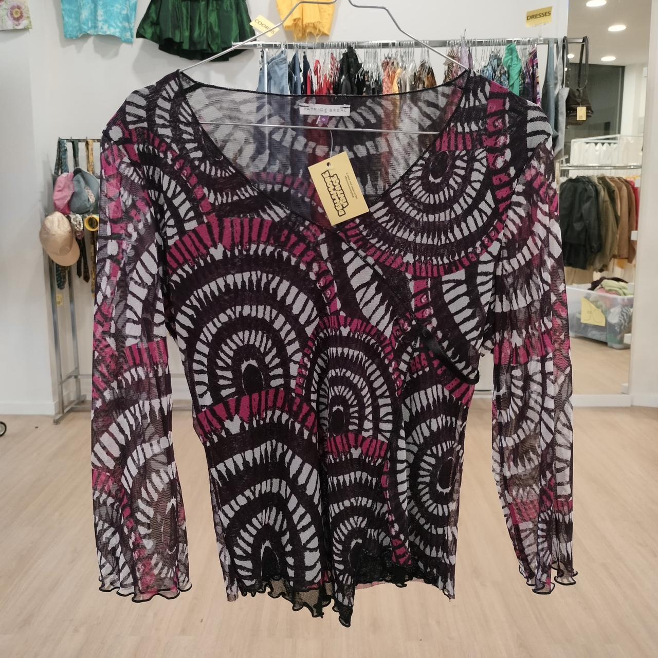 Sheer long sleeve top with black and magenta geometric pattern, hanging in thrift store