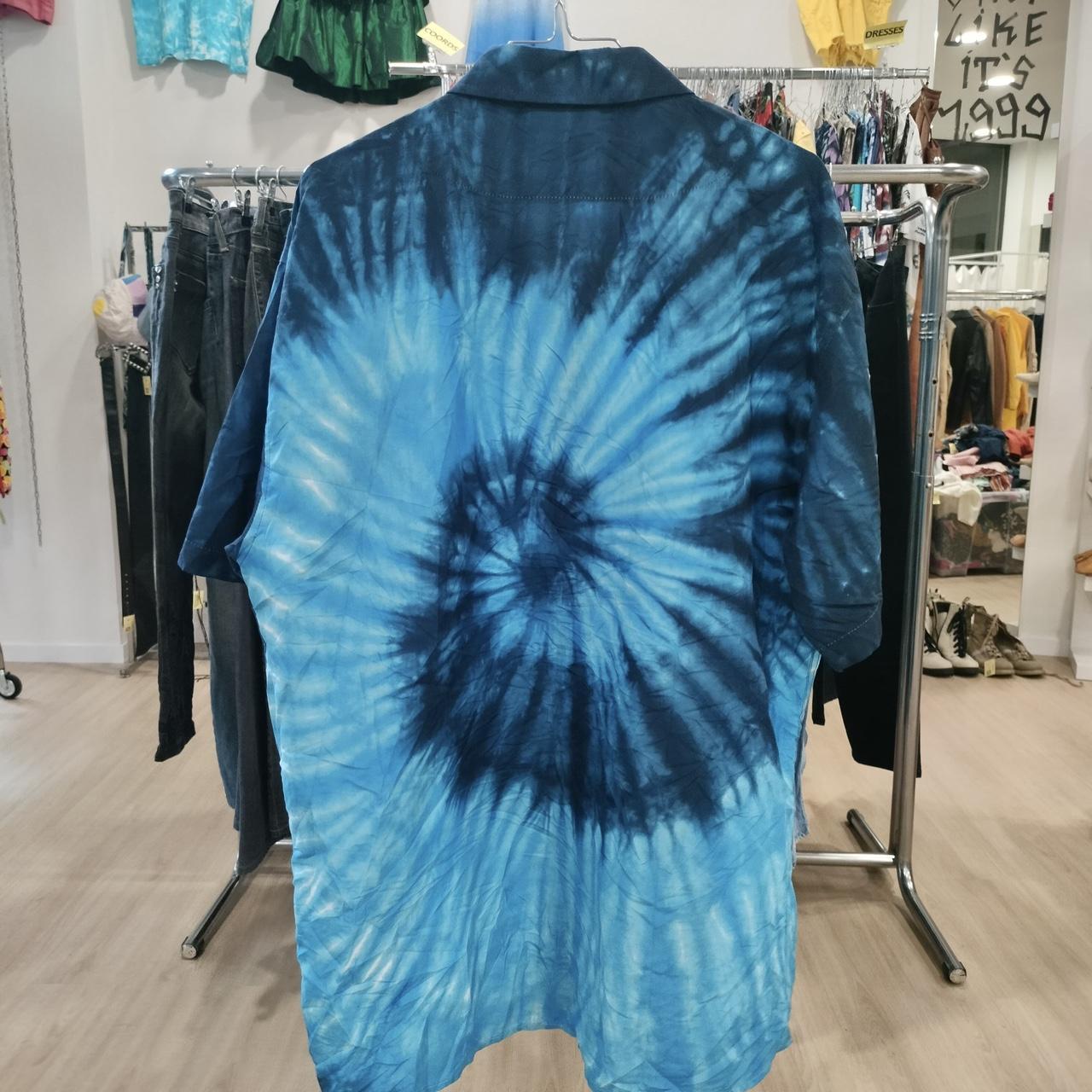 Blue tie-dye shirt with spiral pattern hanging in a vintage clothing store