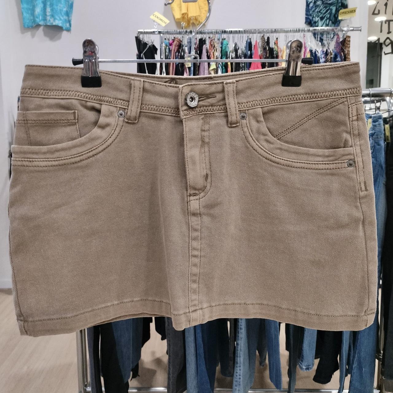 Beige denim mini skirt with front pockets hanging on a rack in a second hand fashion store