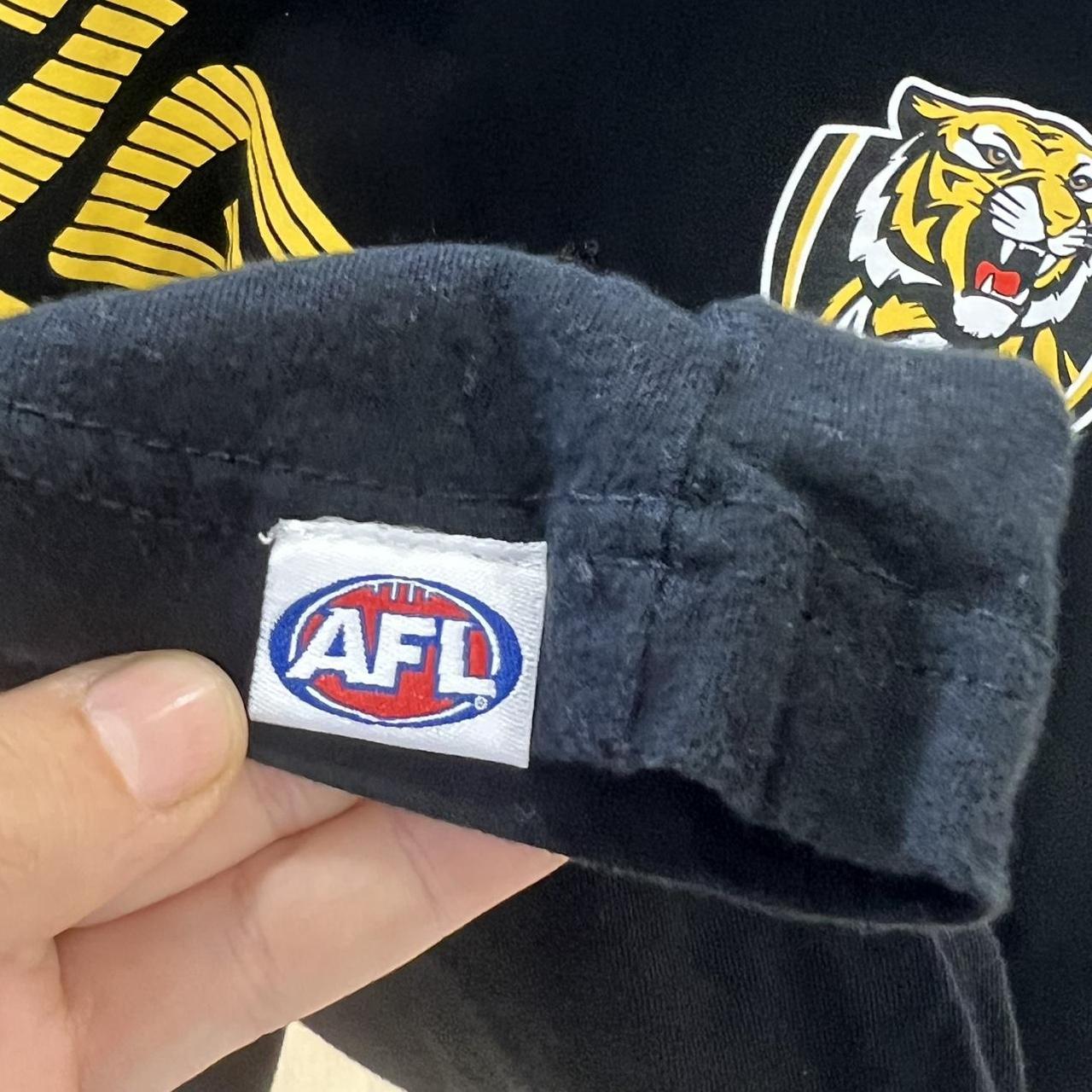 Black t-shirt close-up with AFL logo held by a hand, featuring a tiger emblem in the background