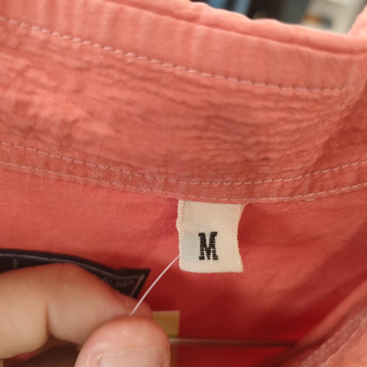 Close-up of a pink garment with a 'M' label held by a hand