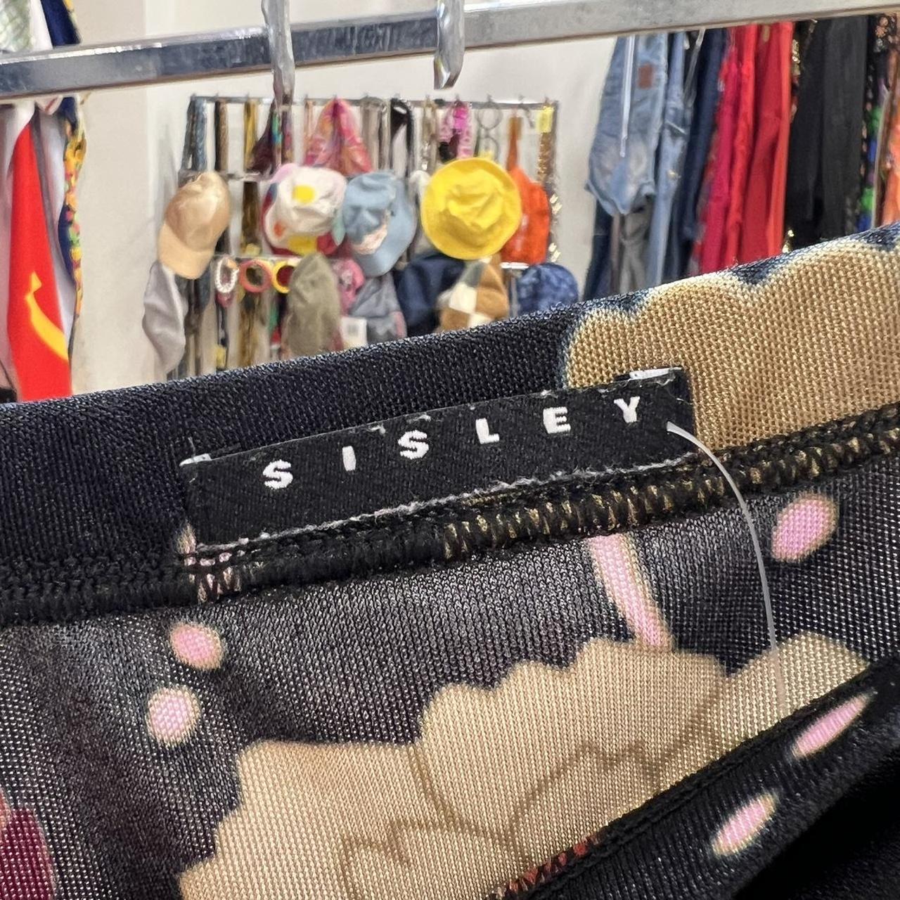 Close-up of a Sisley label on a patterned fabric with a clothing rack in the background