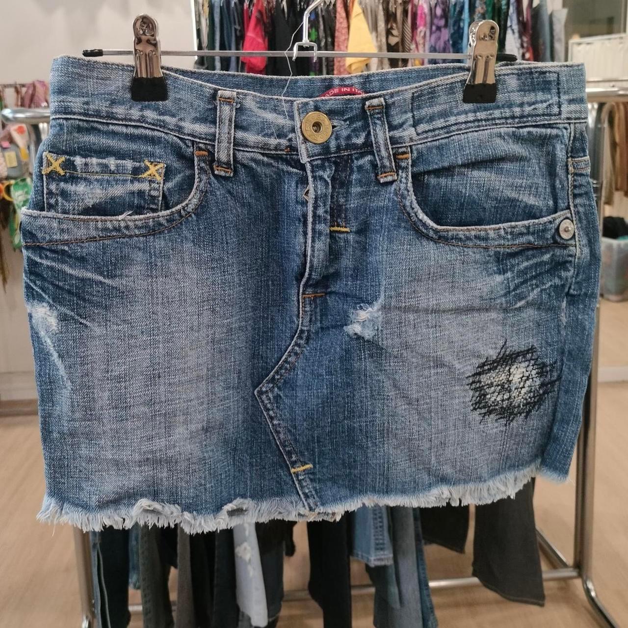 Distressed denim mini skirt with frayed hem and patchwork detail, hanging in a store