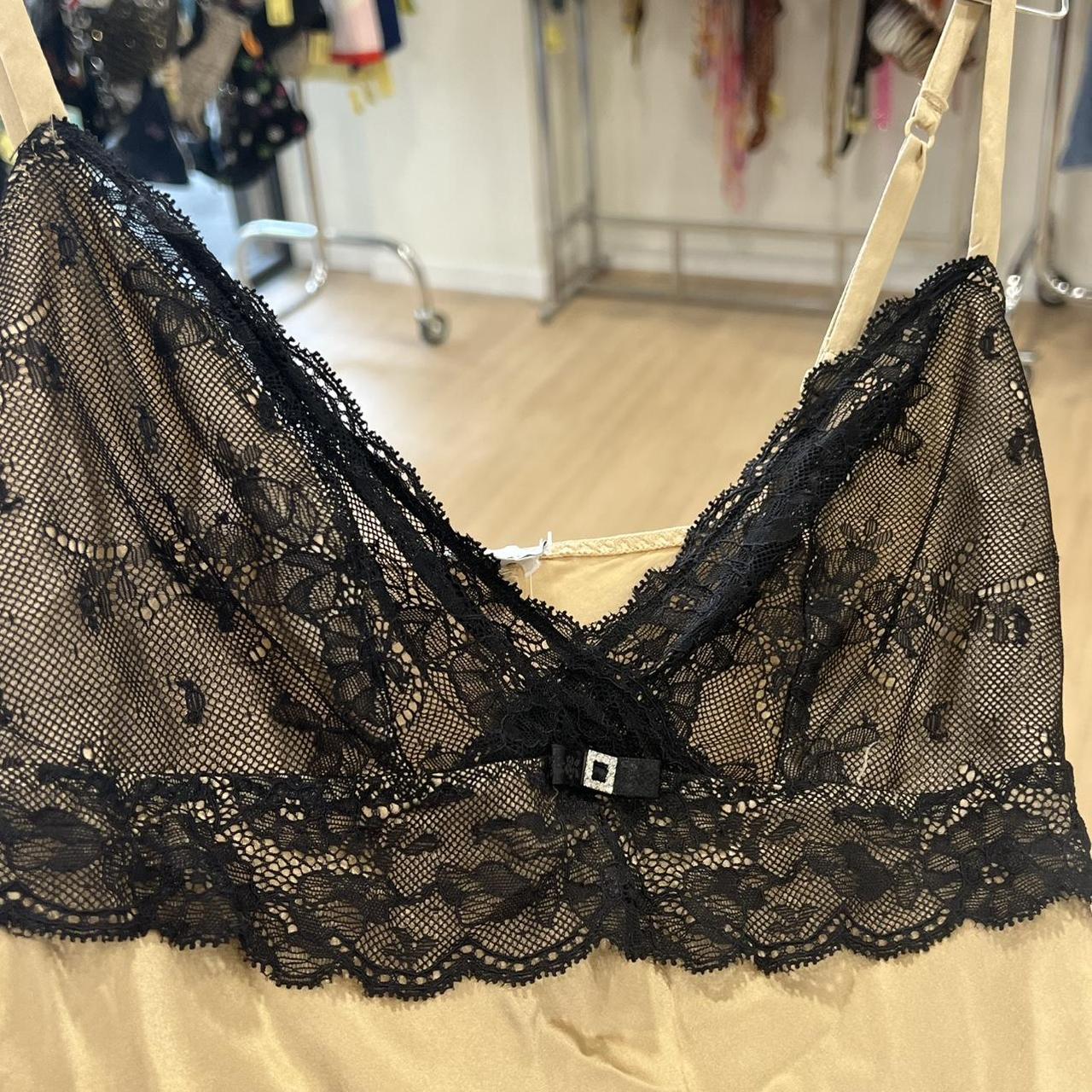 Gold satin camisole with black lace trim and small bow detail, displayed in boutique