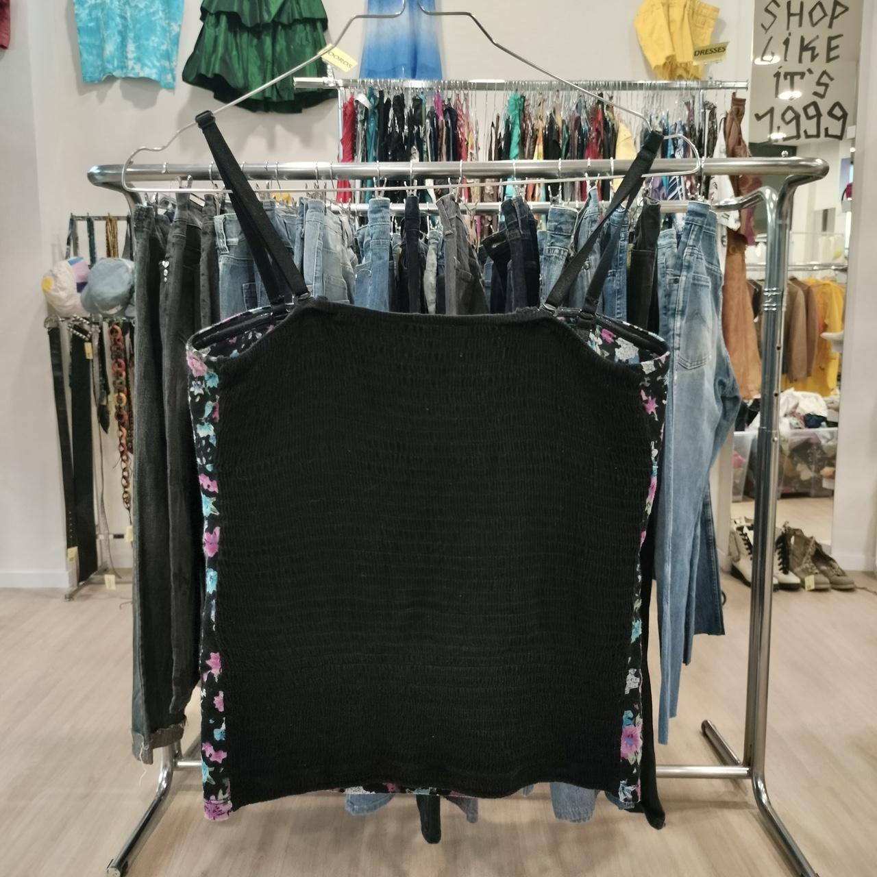 Black smocked tank top with floral side panels on hanger in a vintage clothing store