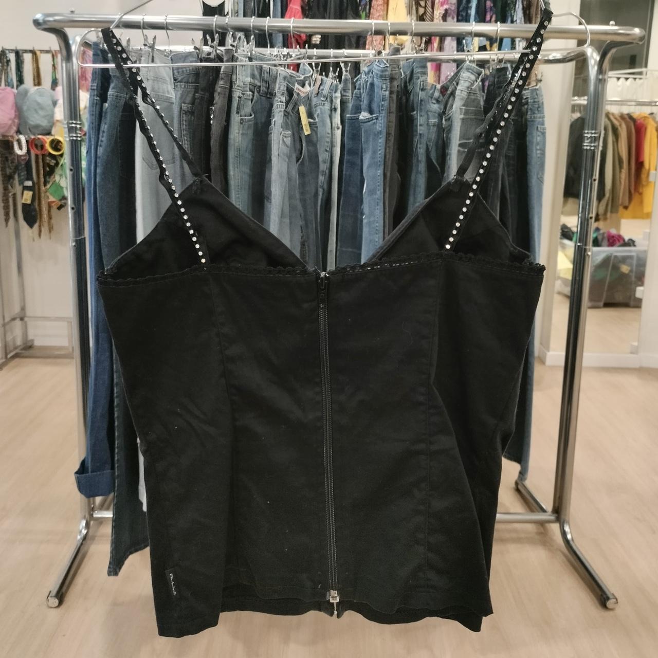 Black zip-up top with thin straps on a clothing rack in a store