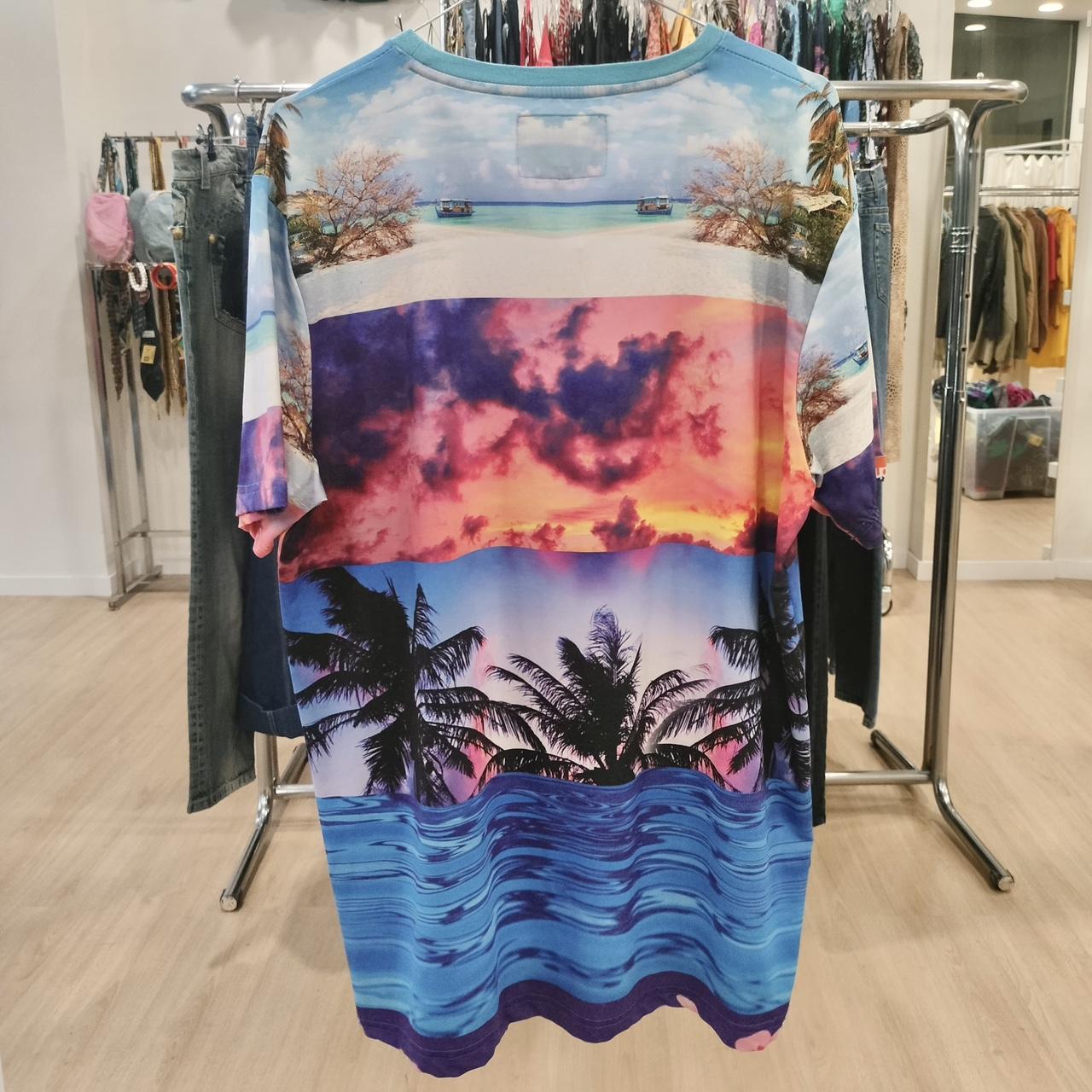 Colorful tropical beach print t-shirt with palm trees, sunset, and ocean, hanging in store