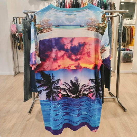 Colorful tropical beach print t-shirt with palm trees, sunset, and ocean, hanging in store