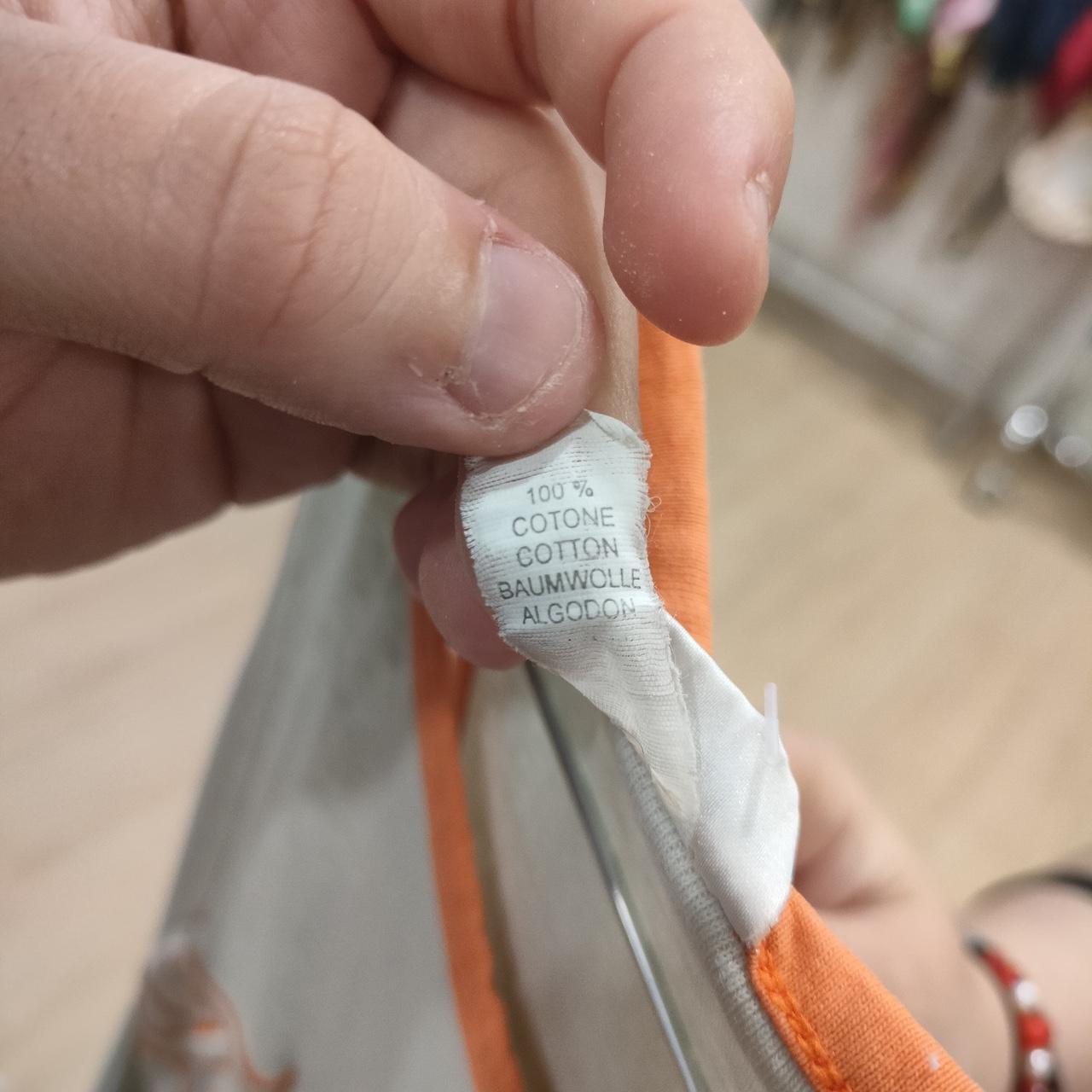 Hand holding a garment with a label showing 100% cotton material, orange trim visible