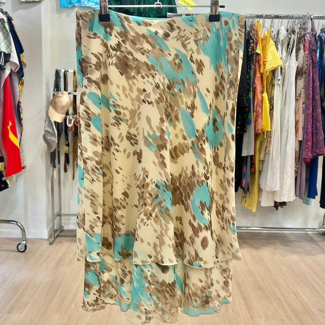 Beige midi skirt with brown and teal abstract pattern, displayed in a secondhand clothing store