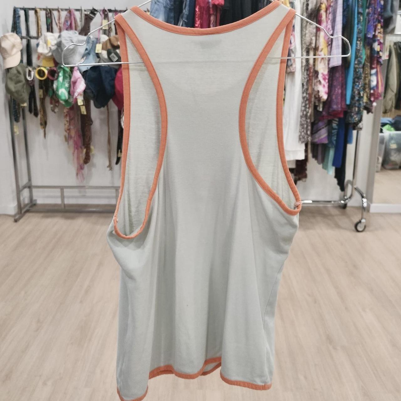 Light grey racerback tank top with orange trim, displayed in a second hand clothing store
