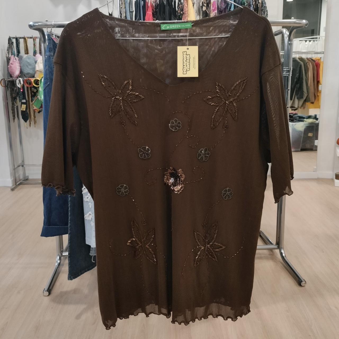Brown sheer blouse with floral embroidery and sequin details, displayed in a boutique.
