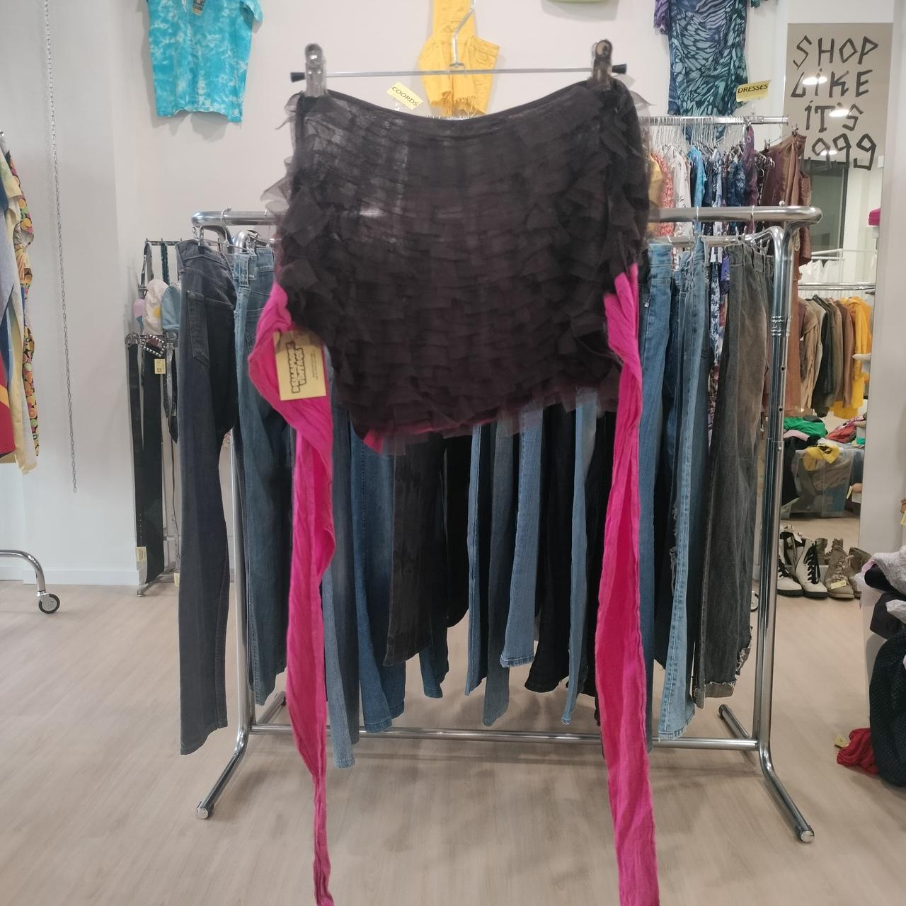 Black layered ruffle mini skirt with pink ties, displayed in a second hand clothing store