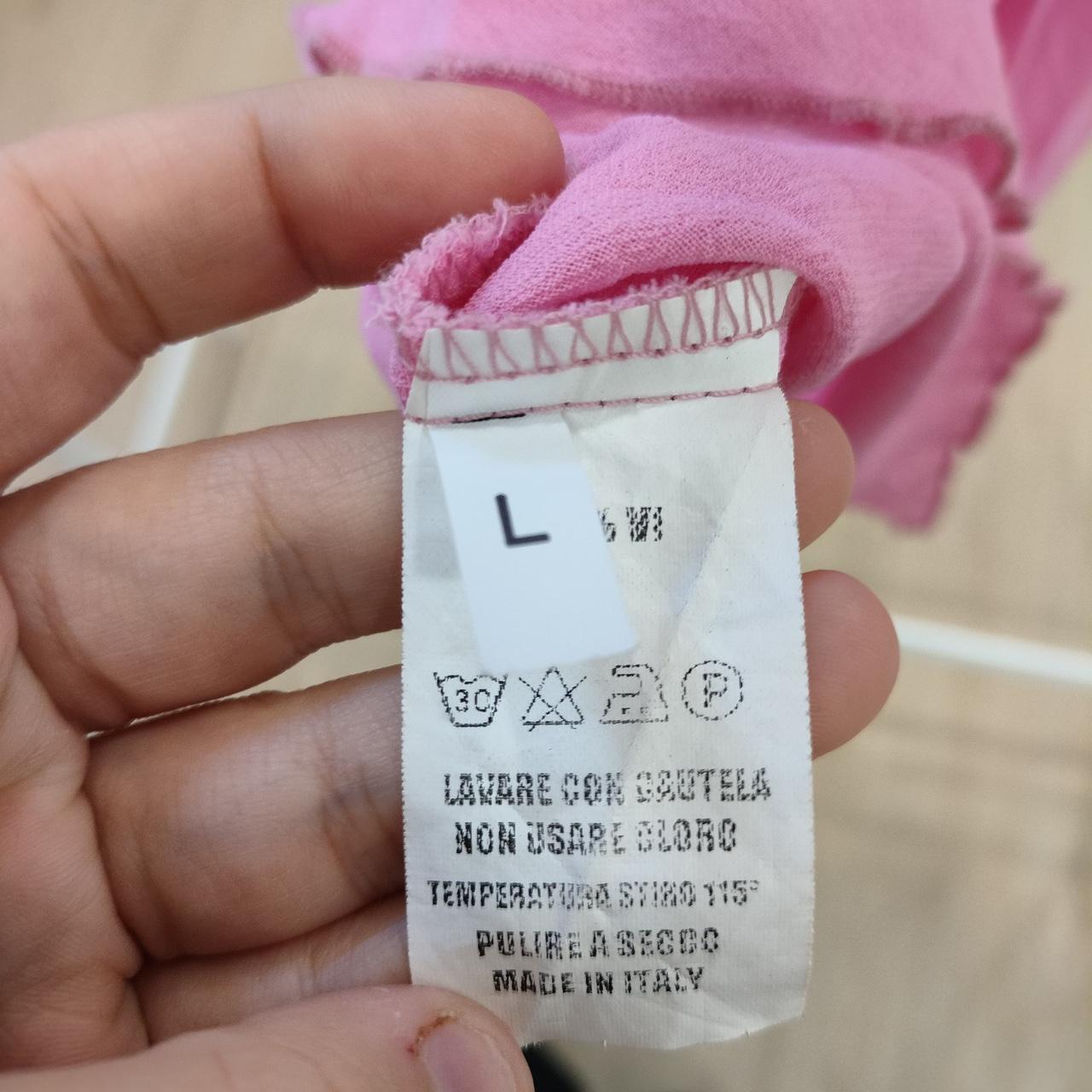 Hand holding a pink garment showing a size L clothing care label, made in Italy.