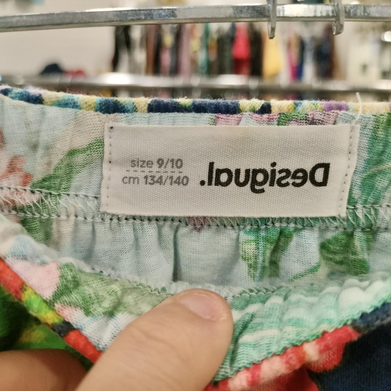 Close-up of a floral fabric with a 'Desigual' label on a clothing rack background