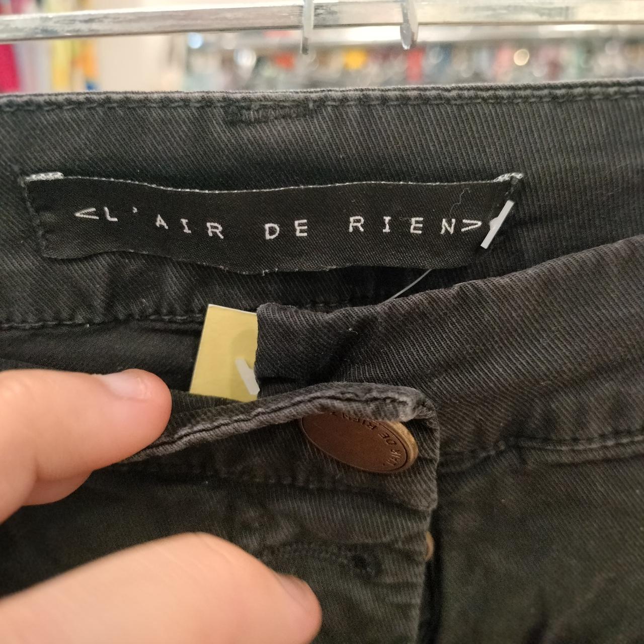 Close-up of black denim jeans waist with L'Air de Rien label and button detail