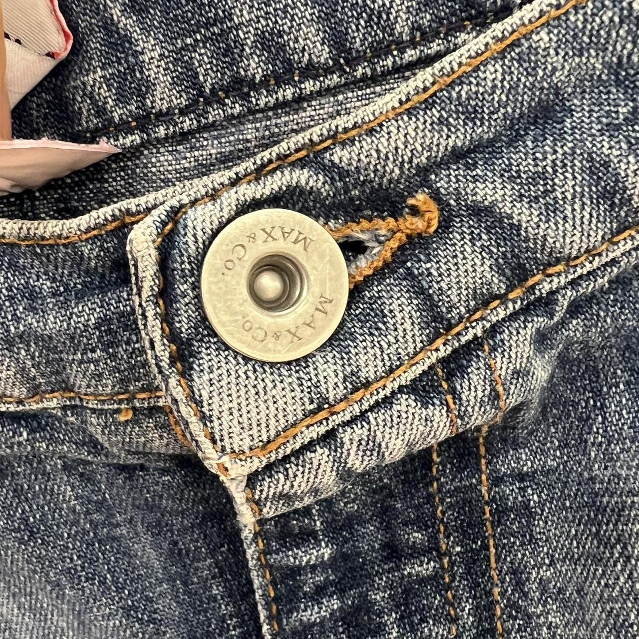 Close-up of a button on a denim jacket with 'MAX&Co.' branding