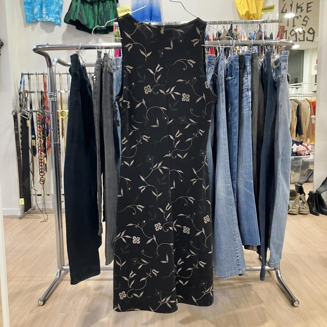 Black floral dress hanging on a rack with jeans and other clothing in a store setting