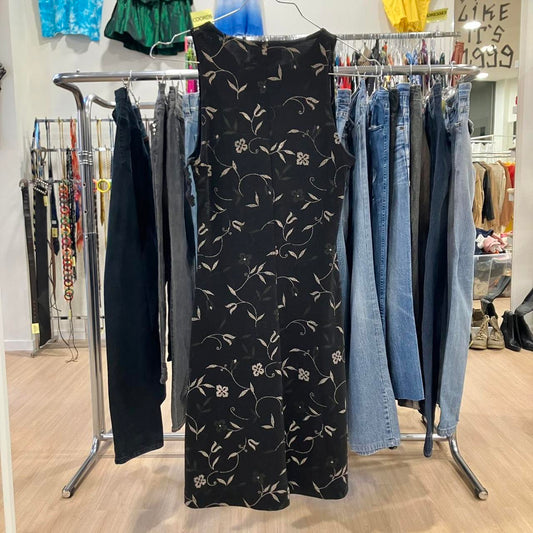 Black floral dress hanging on a rack with jeans and other clothing in a store setting