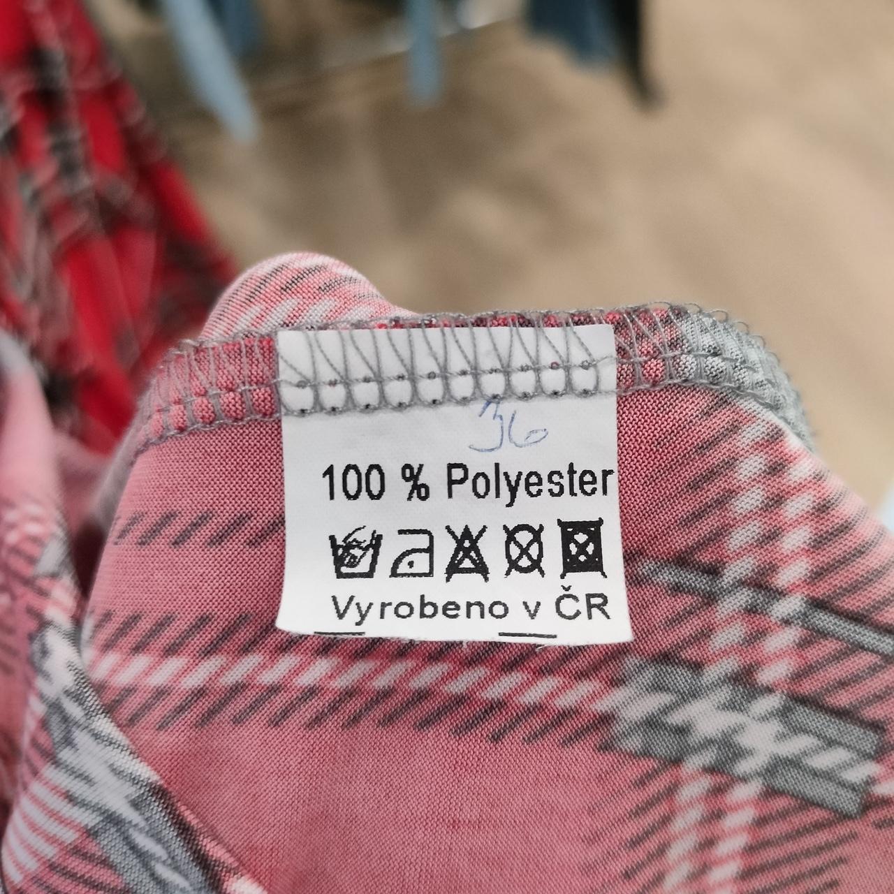Close-up of a 100% polyester plaid clothing label with care instructions and pink fabric