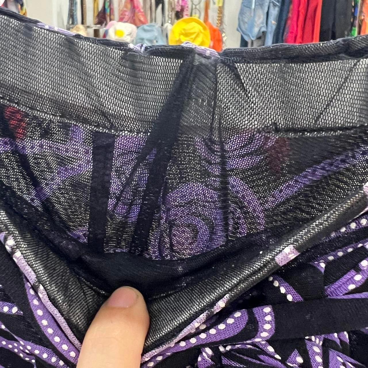 Close-up of a hand holding black mesh fabric with purple patterned detail in a second hand clothing store