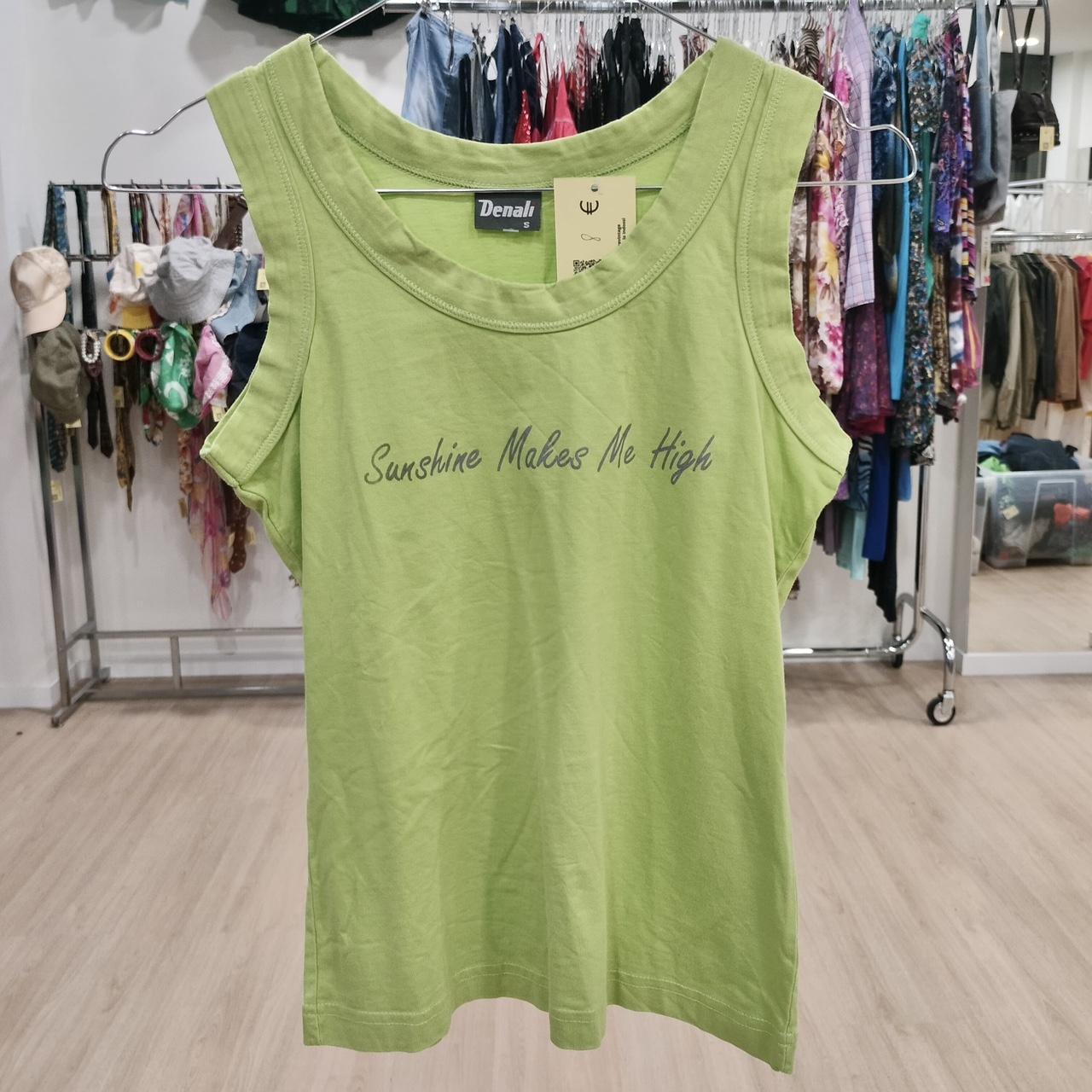 Green sleeveless top with 'Sunshine Makes Me High' text, displayed in secondhand clothing store
