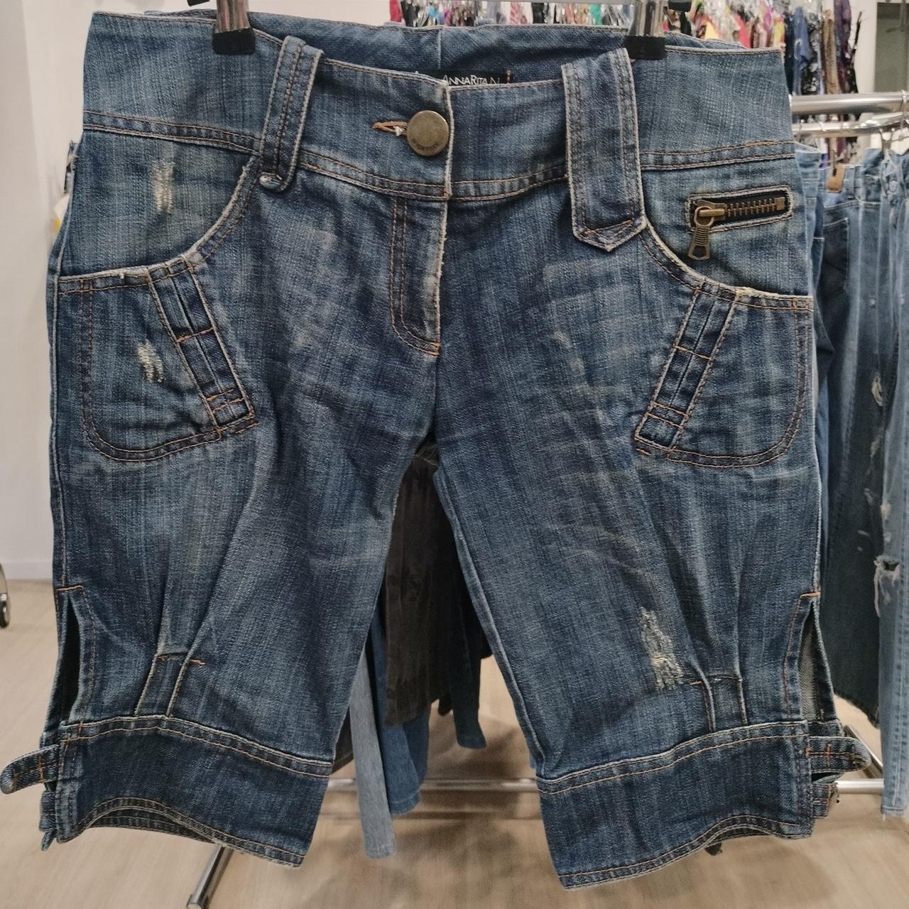 Distressed denim shorts with zipper pocket and side slits hanging on a rack