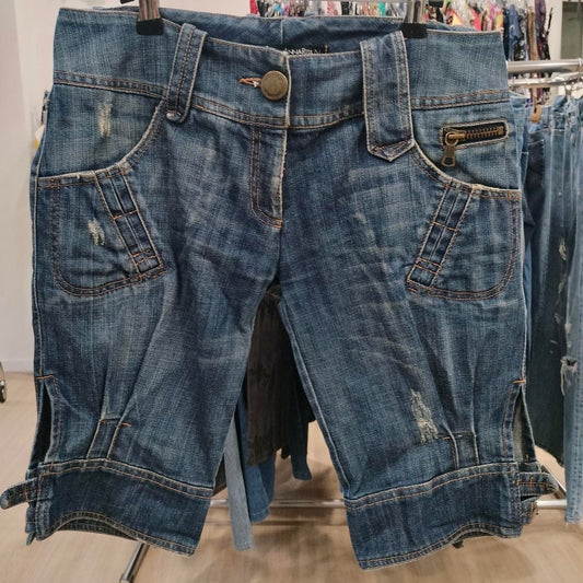 Distressed denim shorts with zipper pocket and side slits hanging on a rack