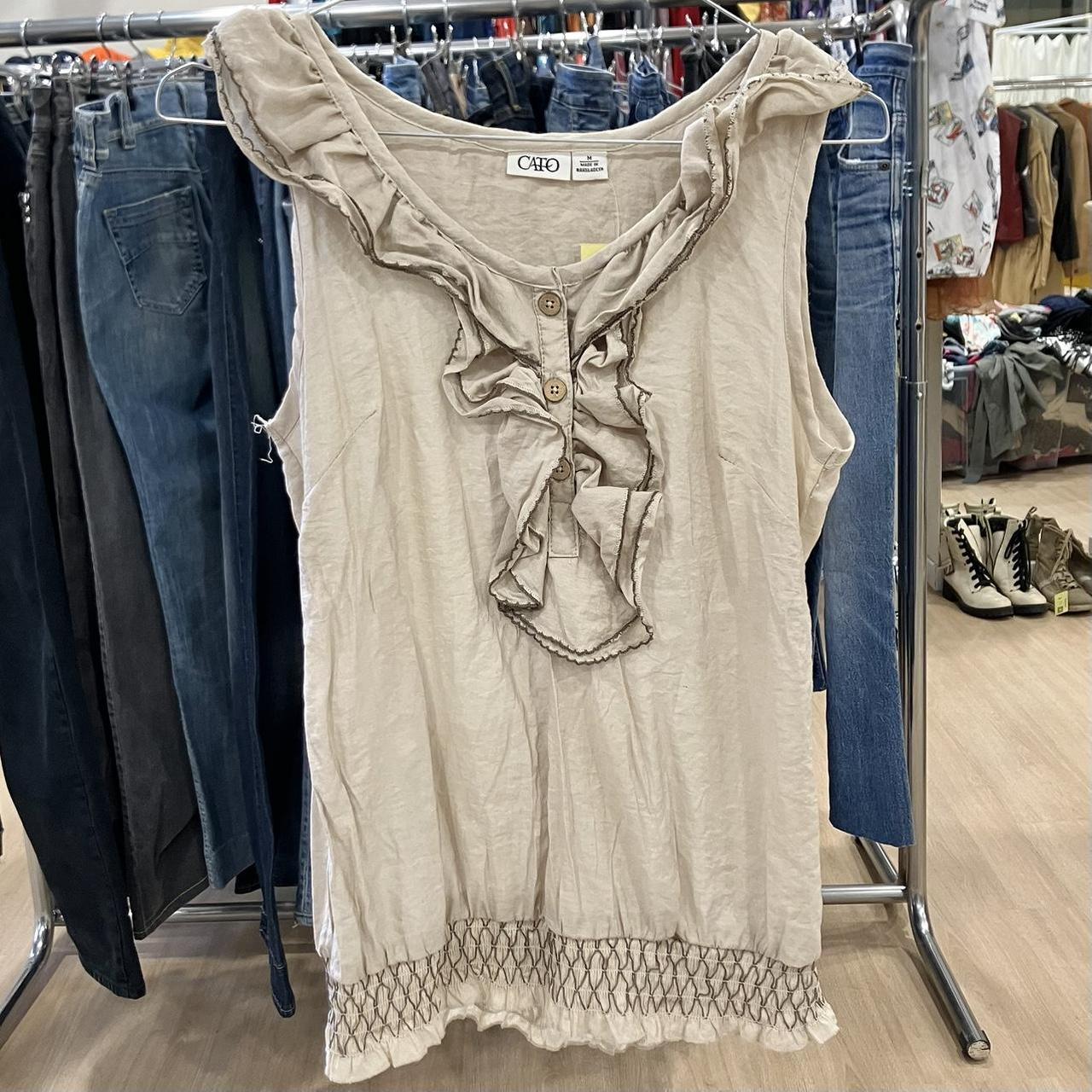 Beige sleeveless ruffle blouse with buttons, displayed in a second hand clothing store