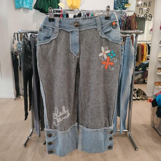Gray denim pants with floral embroidery and button details on a clothing rack