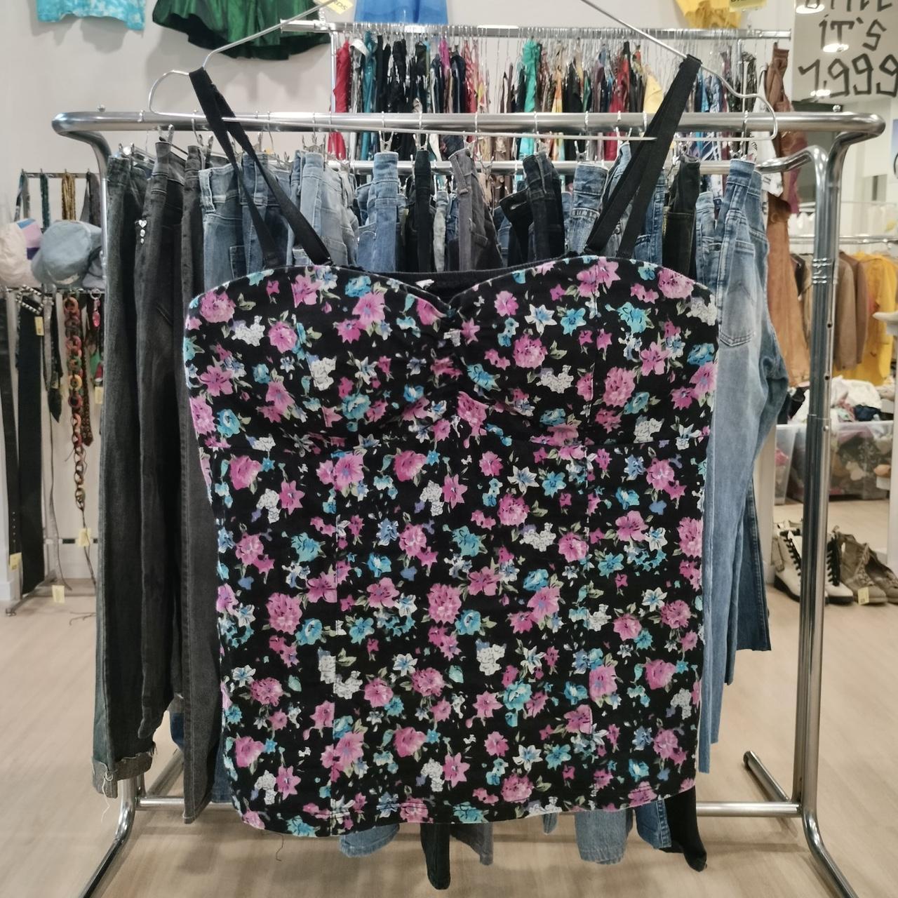 Black floral camisole with pink and blue flowers hanging in second hand clothing store