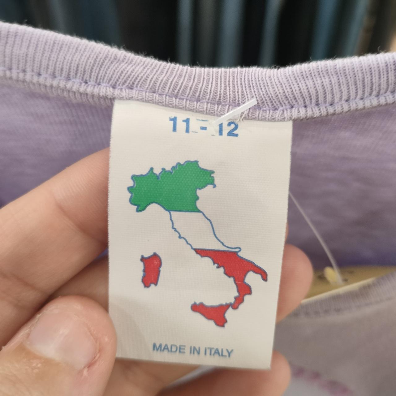 Hand holding clothing tag showing Italian map and 'Made in Italy' on lilac garment