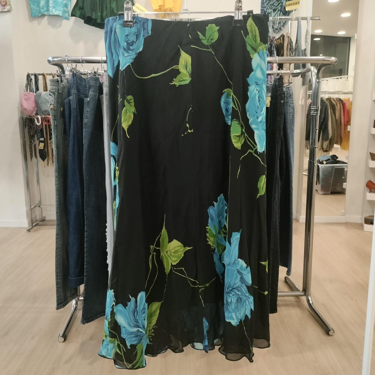 Black maxi skirt with blue floral print and green leaves, displayed in a boutique