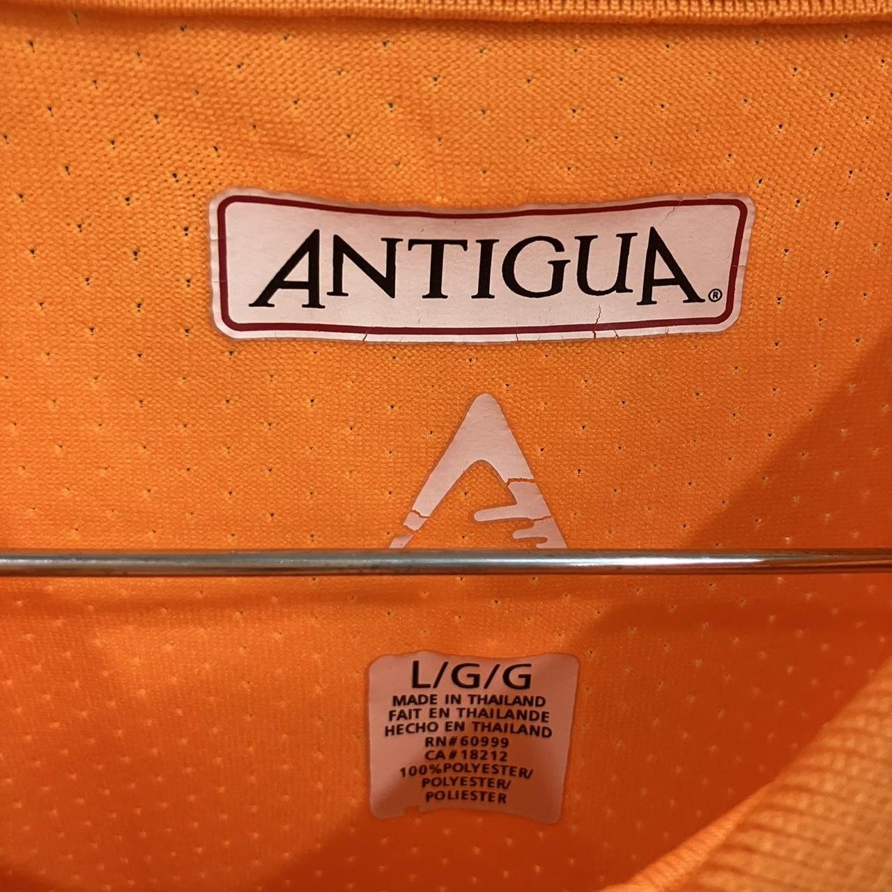 Close-up of a orange polo shirt with Antigua logo and label