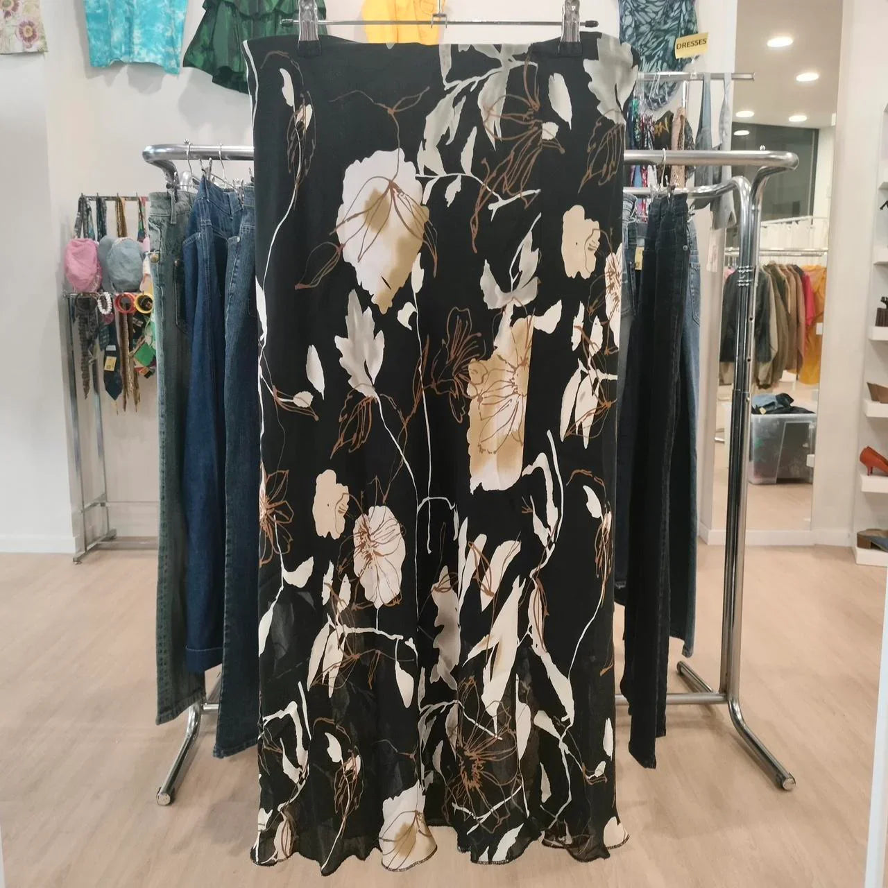 Black floral midi skirt with beige and white flower print, displayed in a second-hand clothing store.