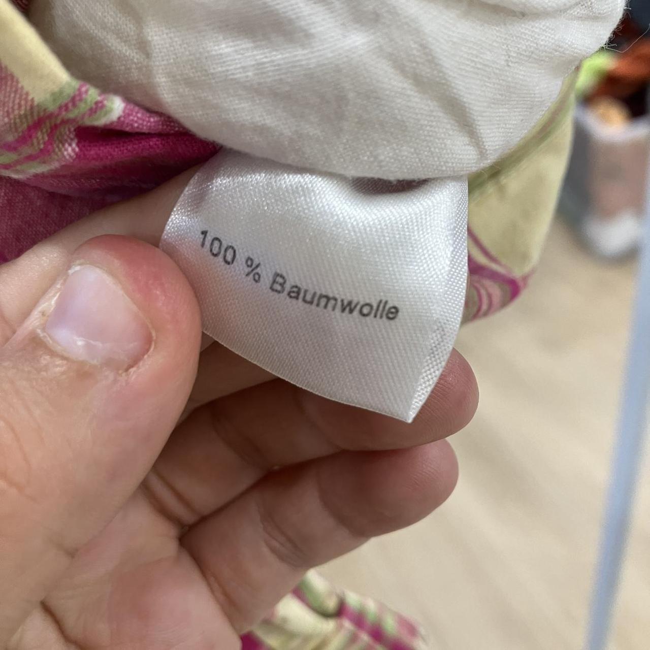 Hand holding clothing care label reading 100% Baumwolle, indicating cotton fabric
