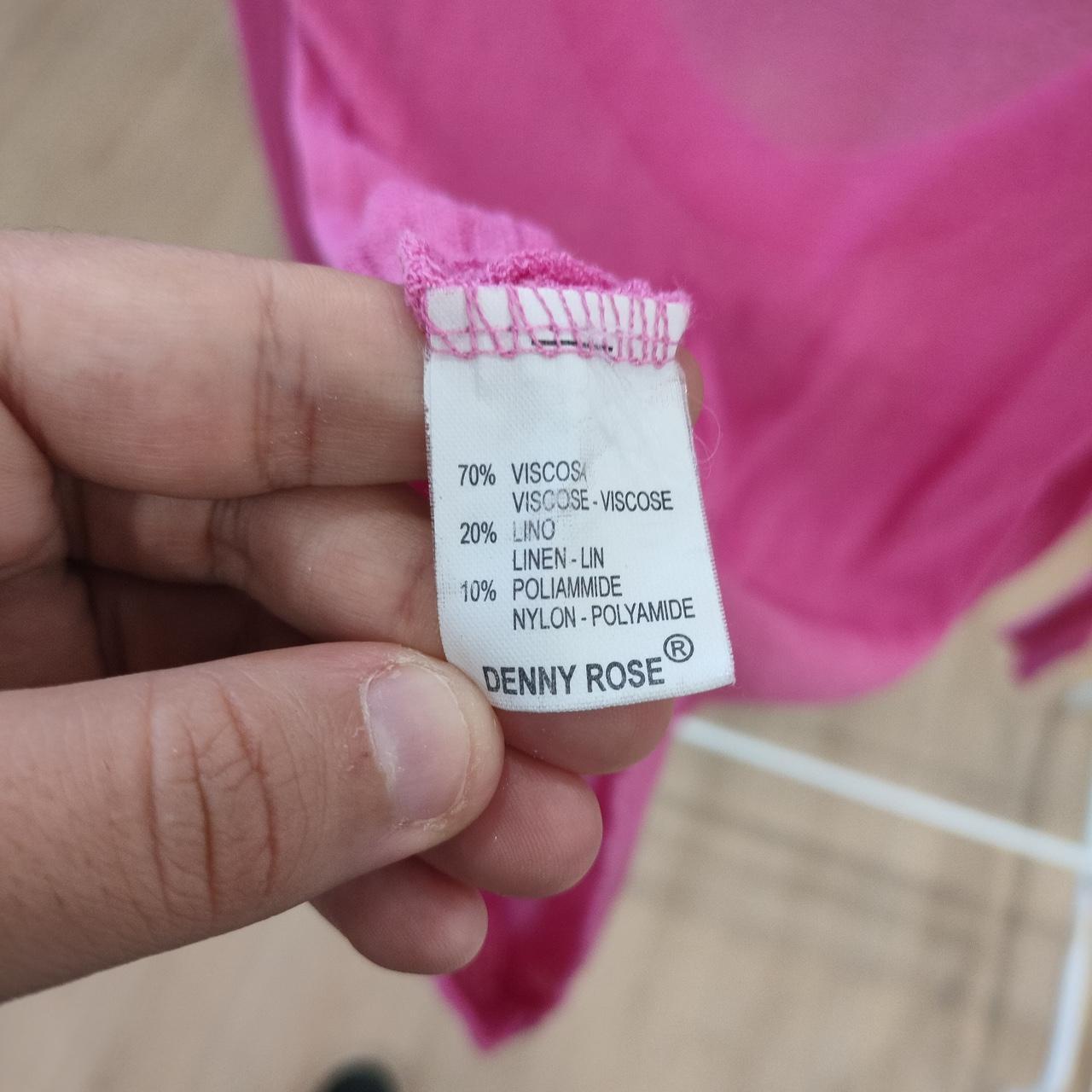 Hand holding a clothing label with 'Denny Rose' brand name against a pink fabric background