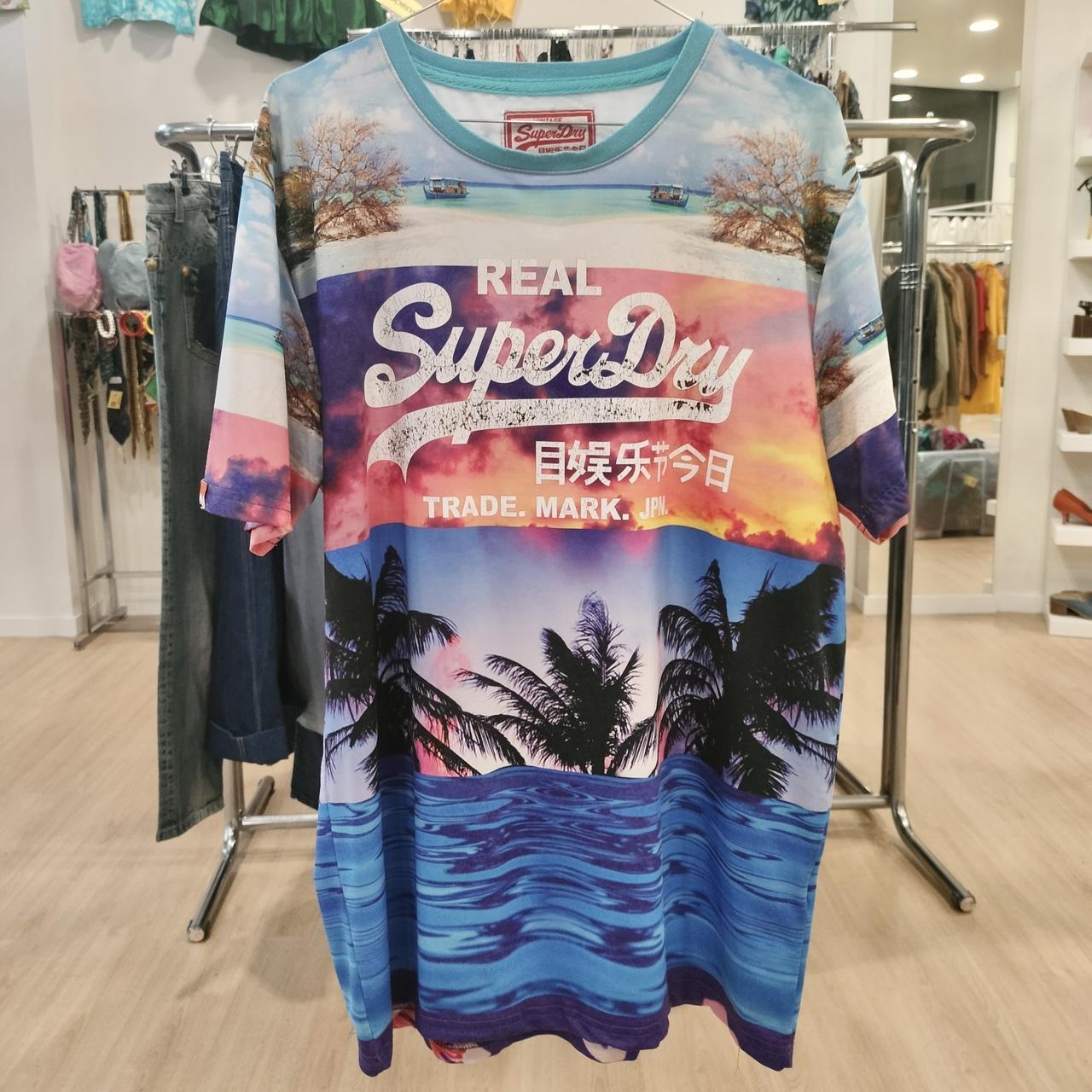 Colorful tropical graphic tee with sunset, palm trees, ocean, and bold text print hanging in store