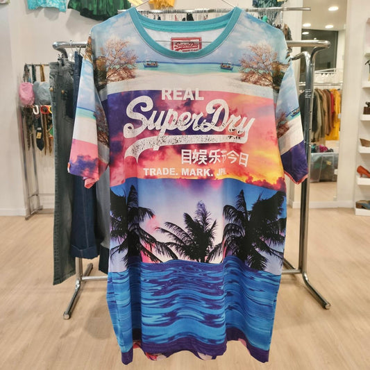 Colorful tropical graphic tee with sunset, palm trees, ocean, and bold text print hanging in store