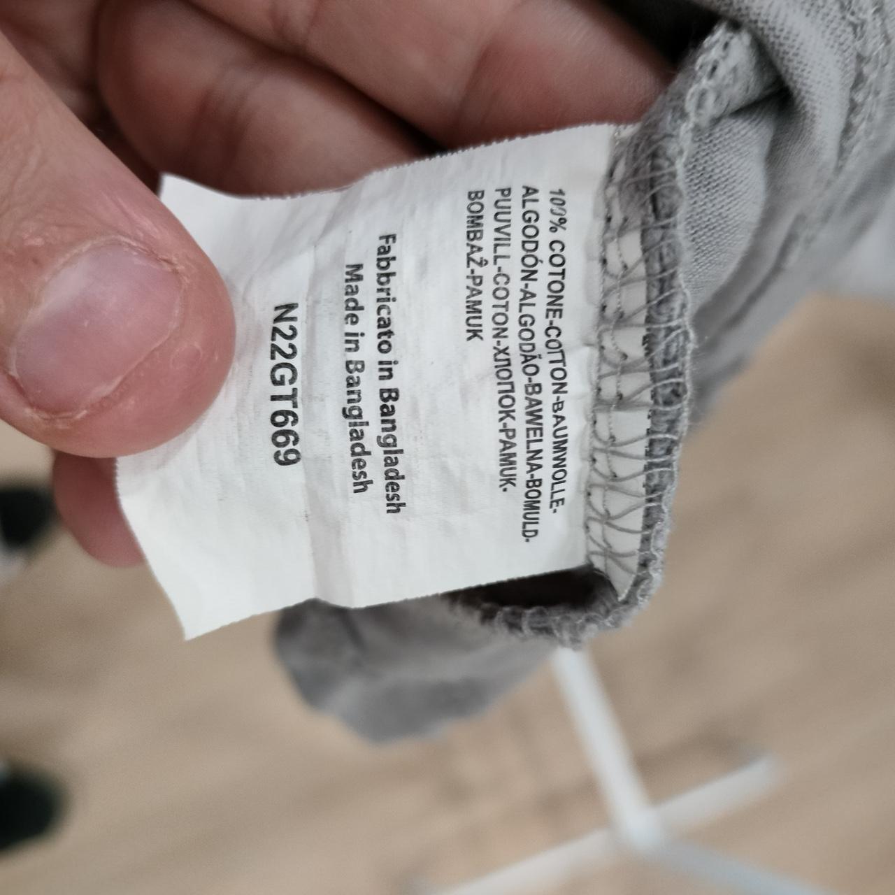 Clothing care tag showing 100% cotton, made in Bangladesh, held by hand