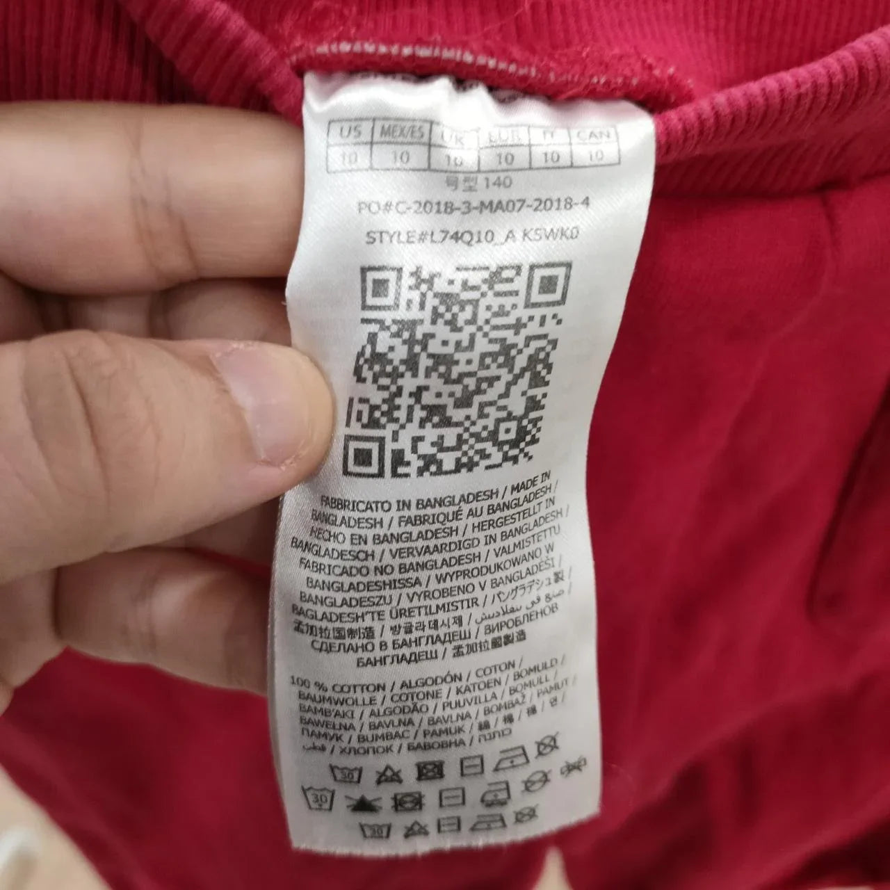 Hand holding red garment with clothing label showing care symbols and QR code